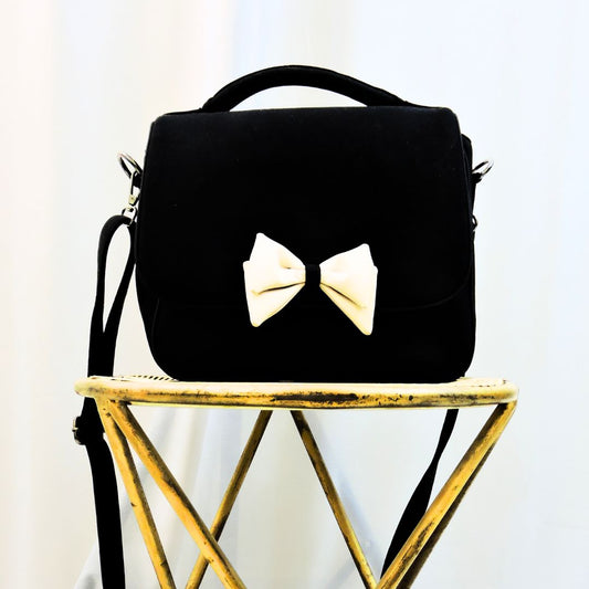 LiveMomma's Pookie Bow-Tie Handbag in Jet Black and Misty Pink with signature bow-tie design, on a wooden stool.